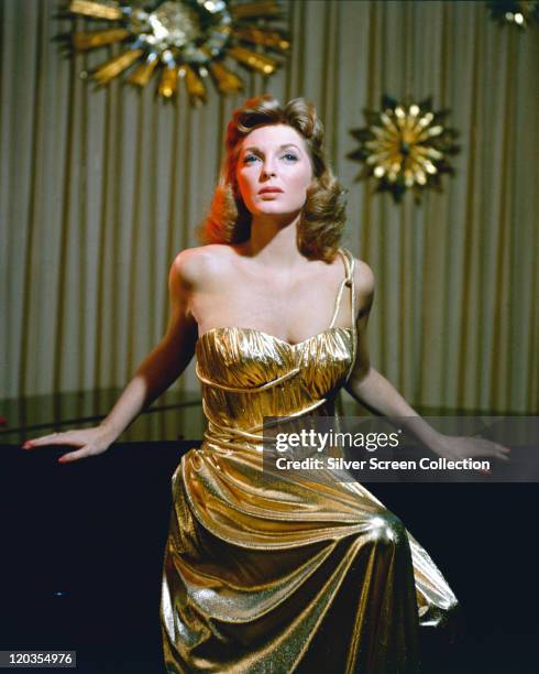 Julie London , US singer and actress, posing beside a grand piano, wearing a gold dress, in a studio portrait, circa 1955.
