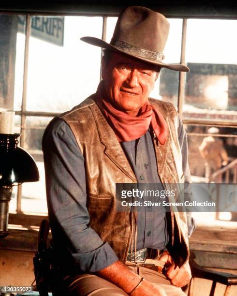 John Wayne , US actor, wearing a cowboy hat, a red neckerchief, a blue shirt and a leather waistcoat in a publicity portrait issued for the film,...
