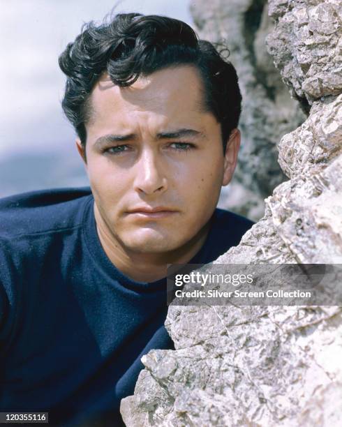 Headshot of John Derek , US actor and film director, poses beside a rockface, circa 1955.