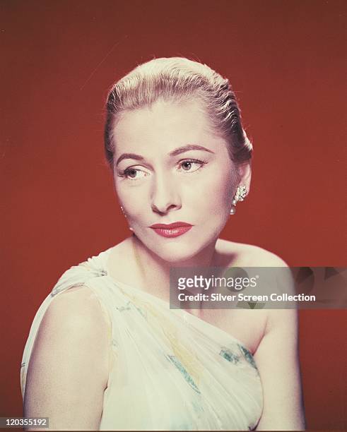 Joan Fontaine, British actress, wearing a white assymetric top in a studio portrait, against a red background, circa 1940.