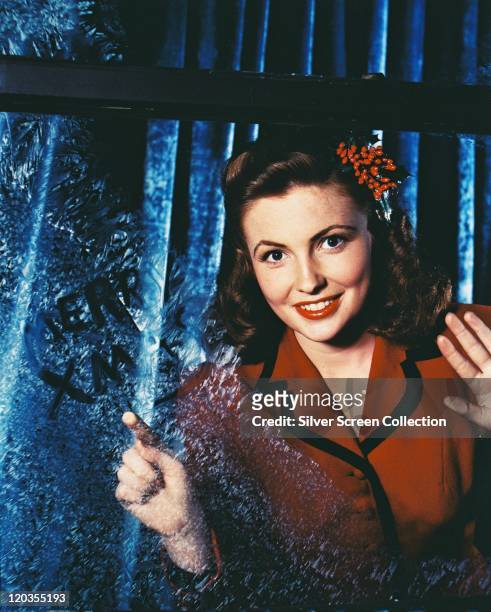Joan Leslie, US actress, wearing a red jacket with black trim, with red berries in her hair, in a studio portrait, circa 1955.