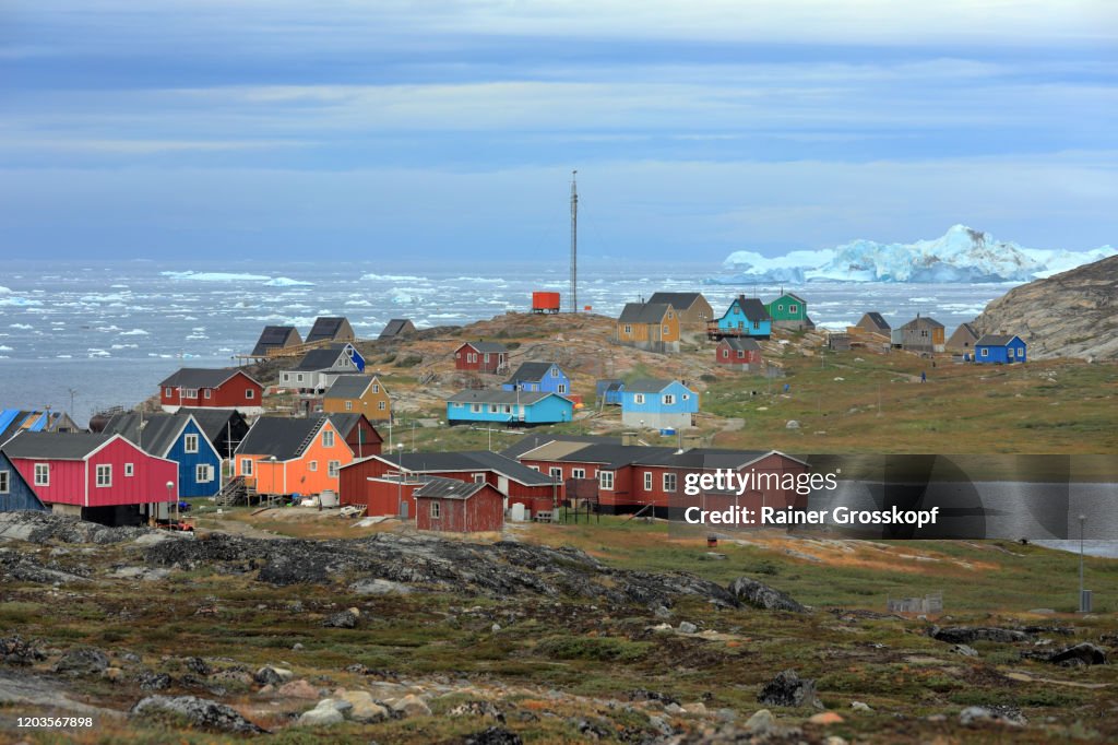 Colorful wooden houses of a tiny little town on a cloudy day with icebergs floating in the sea in the background