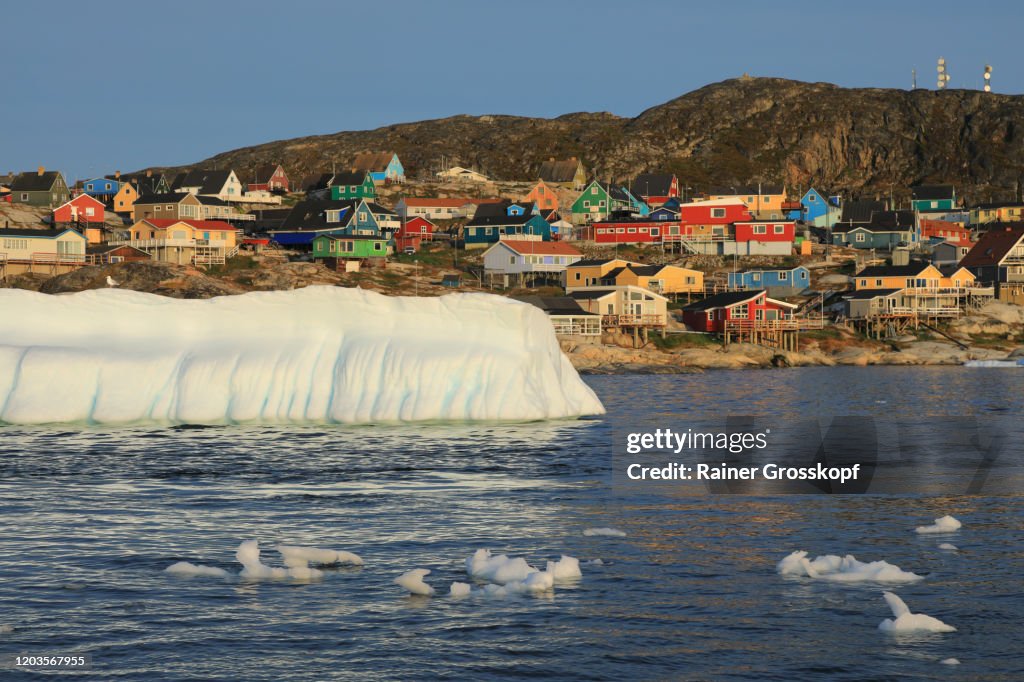 View froom the sea at an iceberg floating in front of colorful wooden houses of a small nordic town