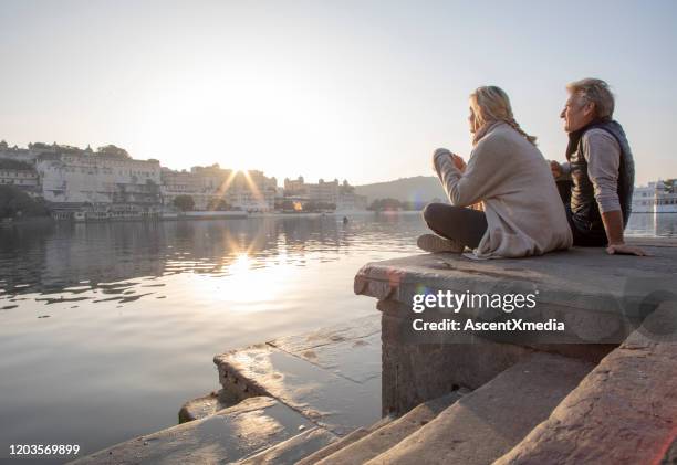 het rijpe paar onderzoekt een ghat bij zonsopgang, kijkt uit over meer terwijl het nippen van hete drank - early retirement stockfoto's en -beelden