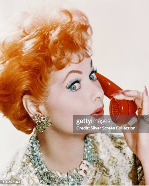 Headshot of Lucille Ball , US comedian and actress, holding a red telephone receiver, in a studio portrait, against a white background, circa 1960.