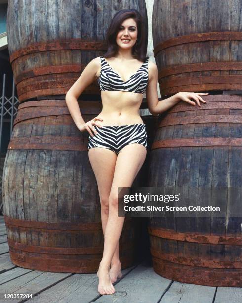 Full-length shot of Linda Harrison, US actress and model, wearing a black-and-white tiger print bikini, posing in front of a stack of wooden barrels,...