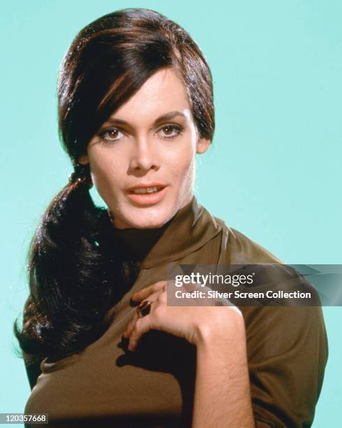 Martine Beswick, British actress and model, wearing a dark green polo neck sweater in a studio portrait, against a light blue background, circa 1965.