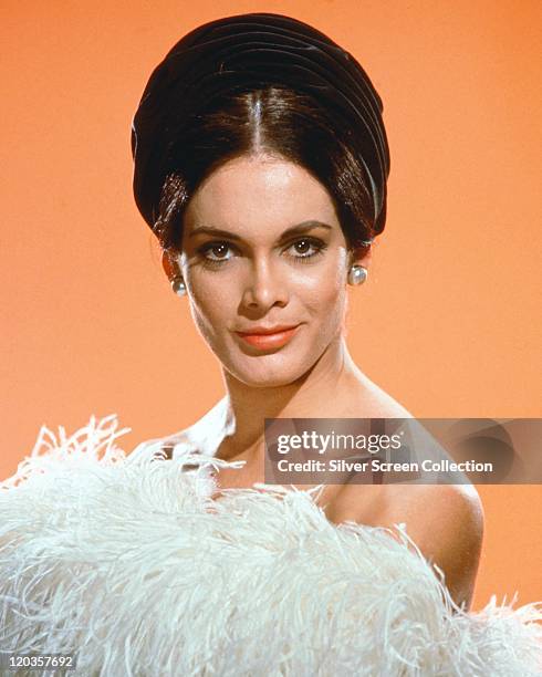 Martine Beswick, British actress and model, wearing a strapless outfit, made of white ostrich feathers, in a studio portrait, against a light orange...