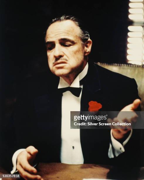 Marlon Brando , US actor, wearing a black dinner jacket with a white shirt and black bow tie, with a red flower on his lapel, in a publicity still...