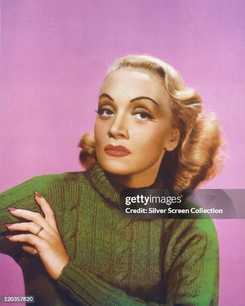 Marlene Dietrich , German actress and singer, wearing a green polo neck jumper in a studio portrait, against a pink background, circa 1940.