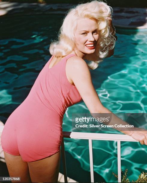 Mamie Van Doren, US actress and singer, wearing a pink swimsuit, leaning on a handrail overlooking a swimming pool, circa 1955.