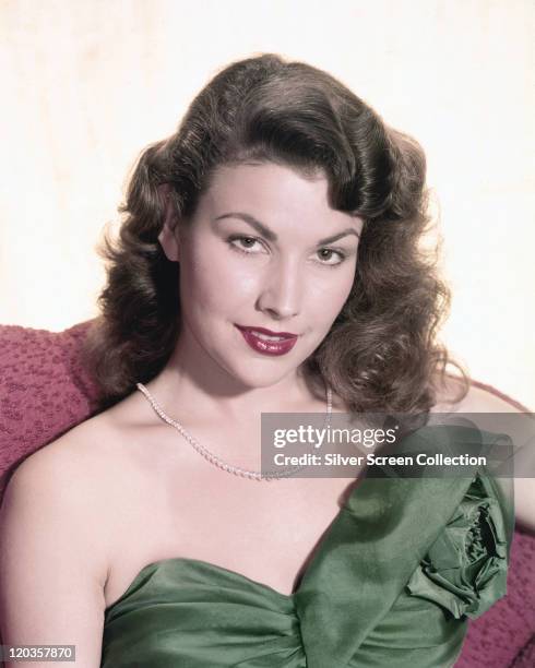 Mara Corday, US actress, wearing a green shoulderless gown and a pearl necklace in a studio portrait, against a white background, circa 1955.