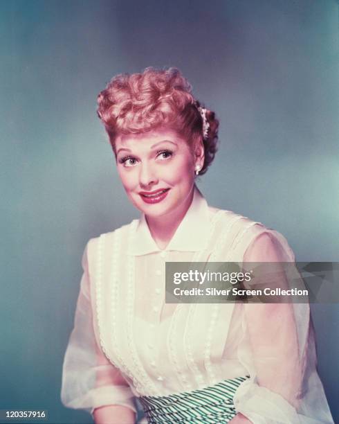 Lucille Ball , US actress and comedian, wearing a white blouse with white chiffon sleeves in a studio portrait, against a grey background, circa 1955.