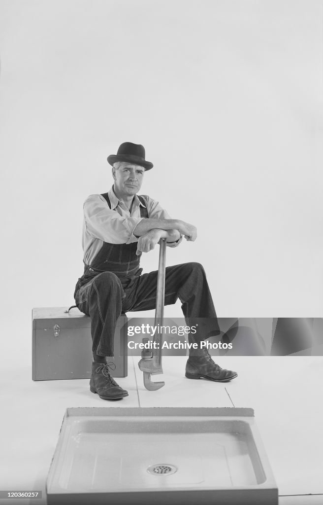 Man sitting on toolbox with adjustable wrench on white background, portrait 