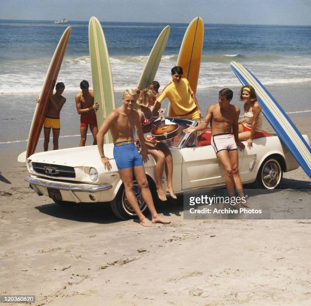 Group of surfers on a beach with a Ford Mustang car.