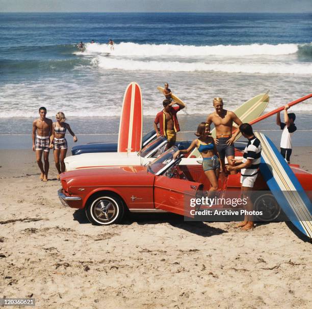 Group of surfers on a beach with a Ford Mustang car.