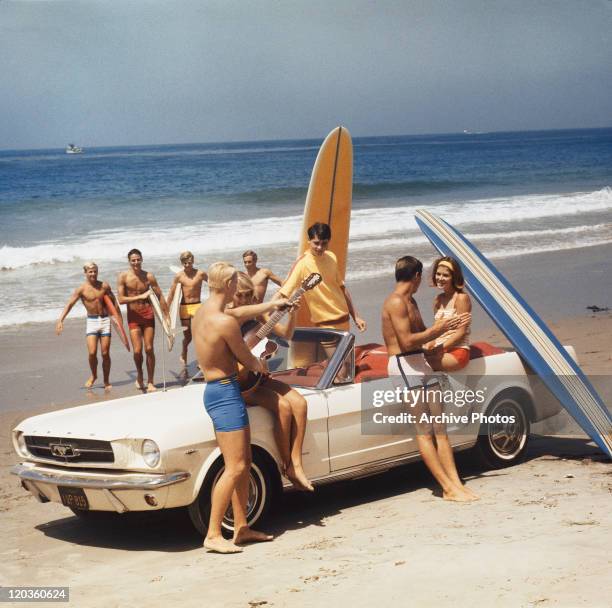 Group of surfers on a beach with a Ford Mustang car.