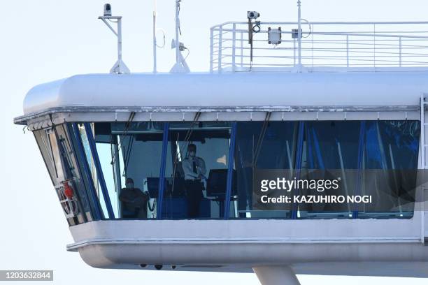 Crew members aboard the Diamond Princess cruise ship are seen at its wheelhouse at the Daikoku Pier Cruise Terminal in Yokohama port on February 27,...