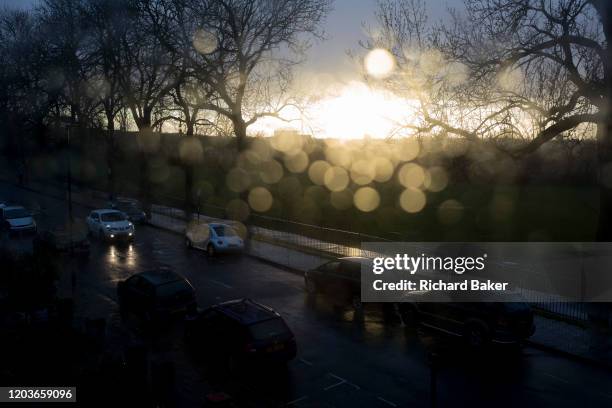 An aerial view of parked cars on a south London street, flooded by sunlight after heavy rainfall with out-of-focus spots of water on the glass of a...