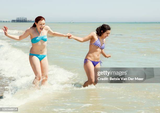 female friends laughing while splashed by waves. - ankle deep in water stock pictures, royalty-free photos & images