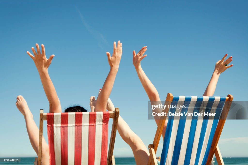 Women throwing arms in air sitting in deckchairs.
