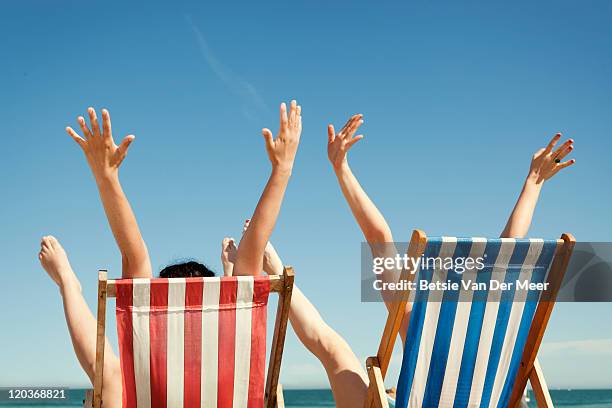 women throwing arms in air sitting in deckchairs. - outdoor chair stock pictures, royalty-free photos & images