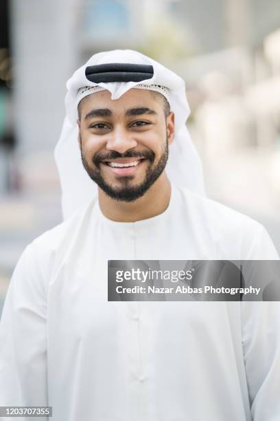 young emirati  man is posing for a close-up portrait looking at the camera and smiling. - united arab emirates culture stock pictures, royalty-free photos & images