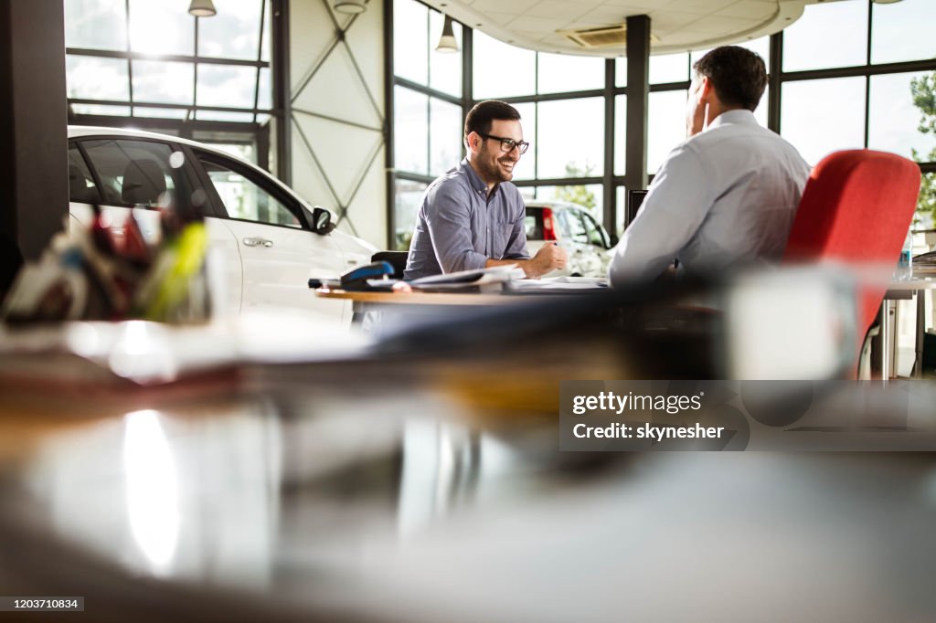 Junger glücklicher Mann im Gespräch mit Autoverkäufer in einem Showroom.