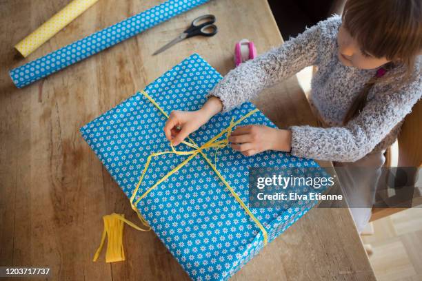 child tying yellow paper ribbon into a bow wrapped around a gift - house presents golf day inside foto e immagini stock