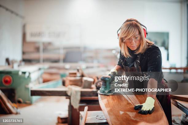 houtbewerker die een handschuurmachine gebruikt om onderaan een houten oppervlakte te schuren - oorbeschermer stockfoto's en -beelden