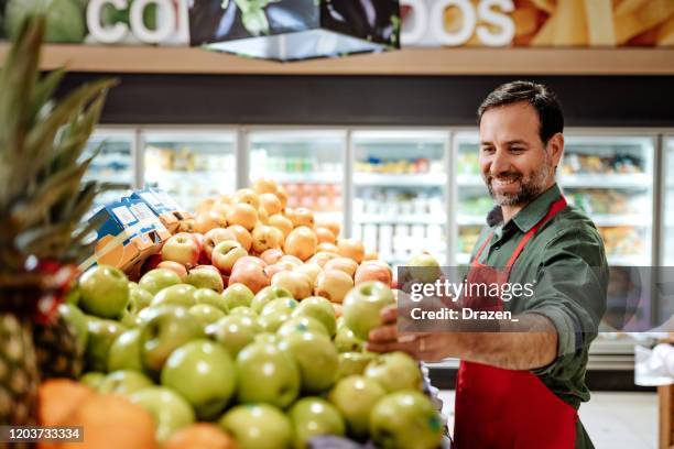 latino werknemer in supermarkt die fruitstapel schikt - retail occupation stockfoto's en -beelden