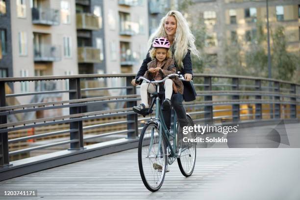 young mother cycling with daughter sitting on her bicycle - copenhagen cycling stock pictures, royalty-free photos & images