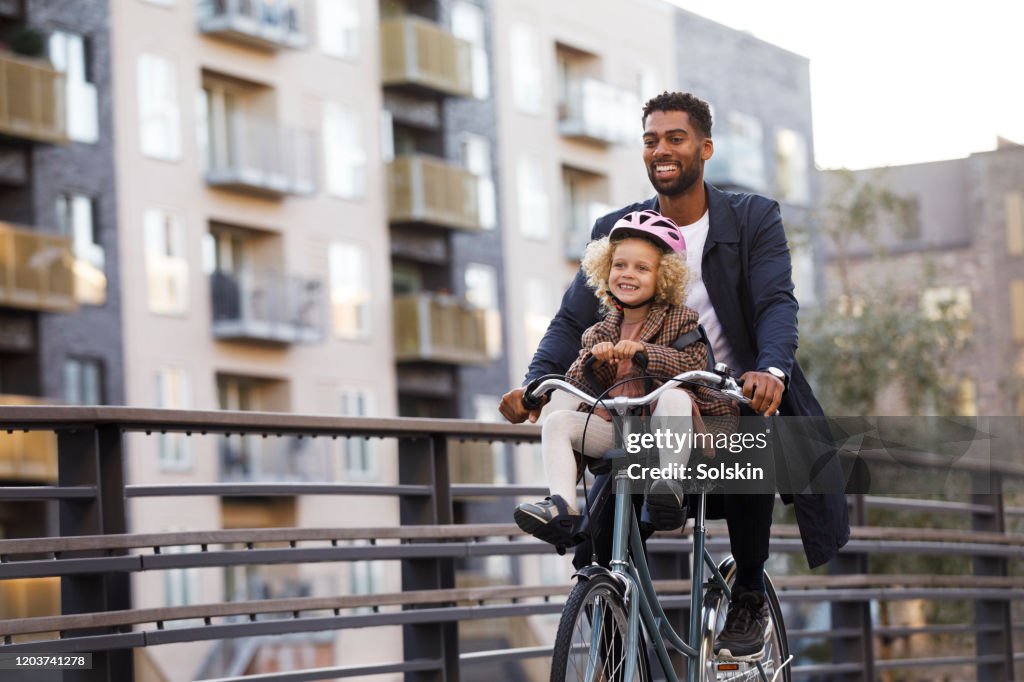 Father cycling with daughter sitting in bicycle seat