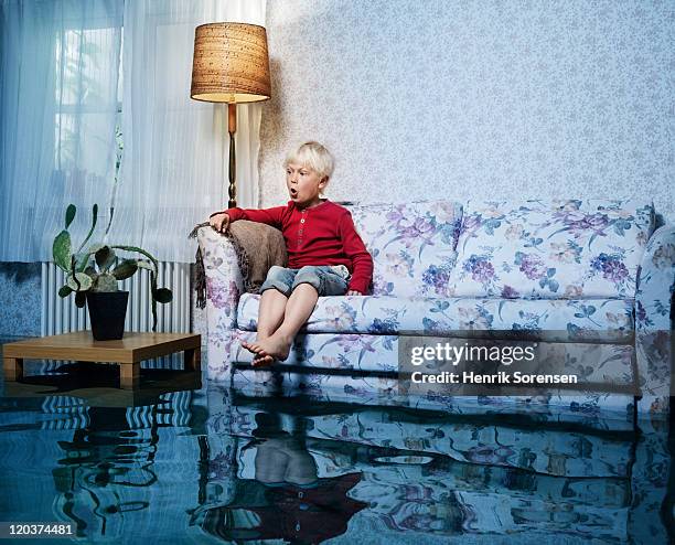 young boy in sofa in flooded room - flooded room stock-fotos und bilder