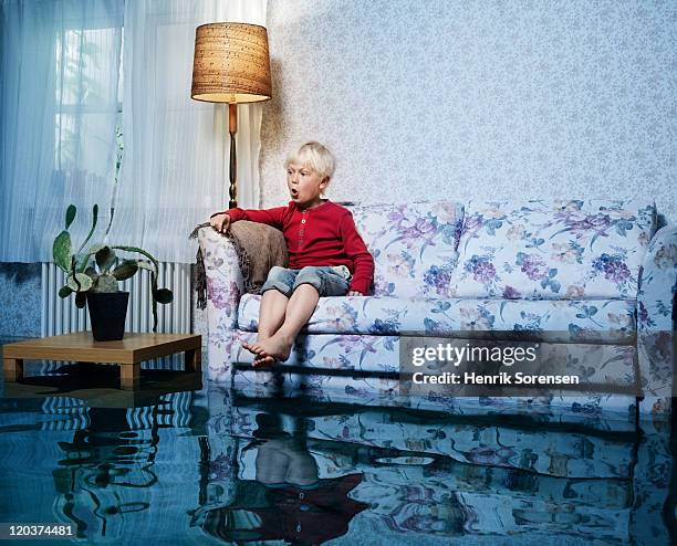 young boy in sofa in flooded room - huis overstroming stockfoto's en -beelden