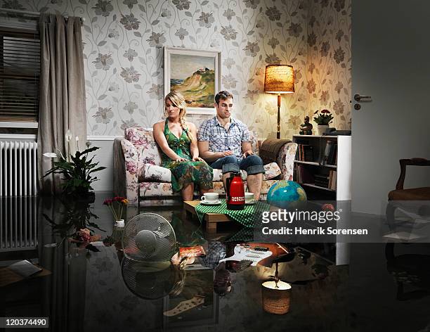 young couple in sofa in a flooded room - damaged stock-fotos und bilder