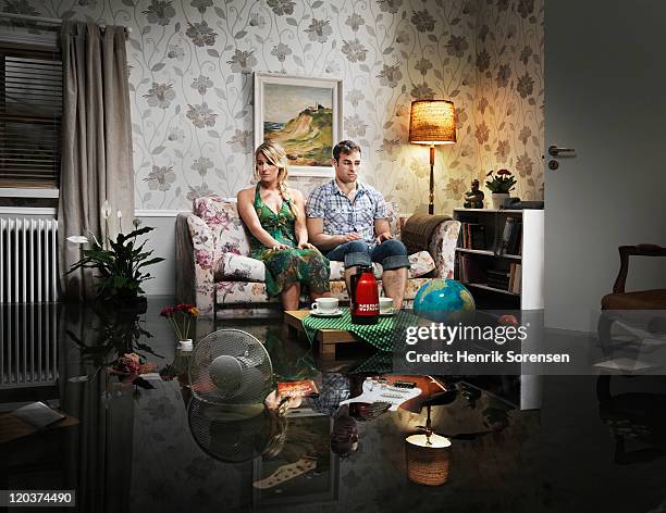 young couple in sofa in a flooded room - vrouw behangen stockfoto's en -beelden