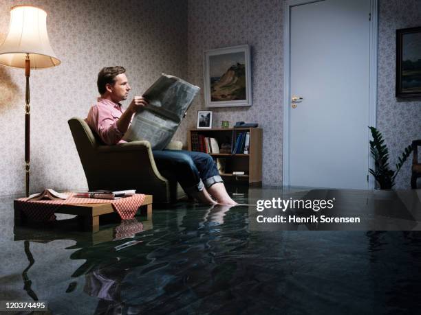 man with newspaper flooded room - ignorancia fotografías e imágenes de stock