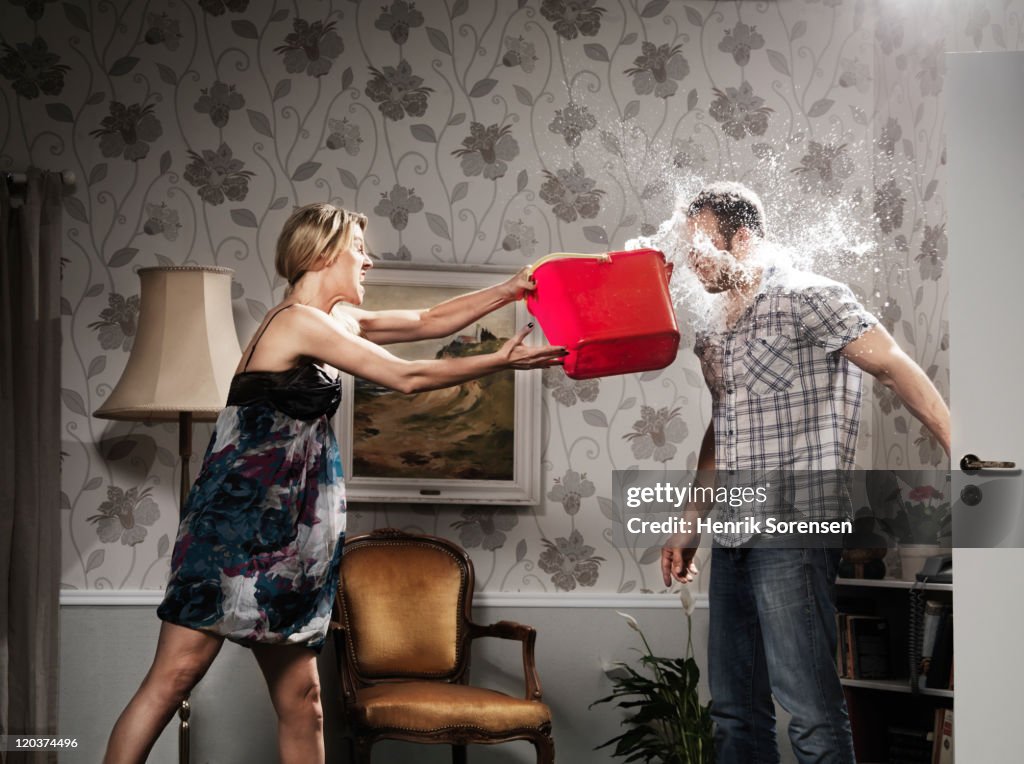 Woman thowing a bucket of water at her partner