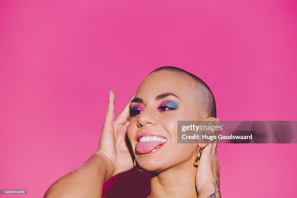 Young happy beautiful woman against a pink background sticking out her tongue.