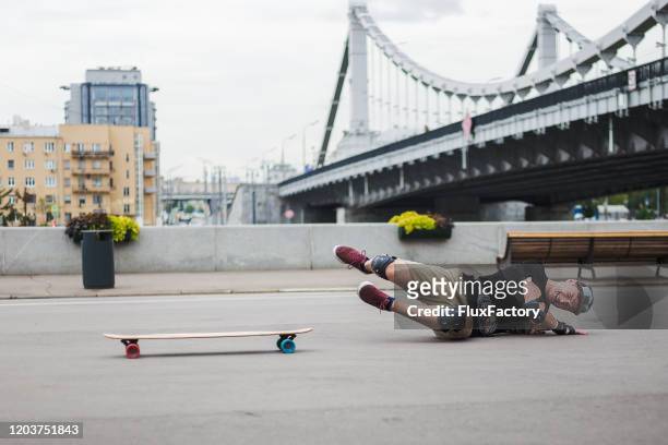 urban young man falling from longboard and hitting the ground - daredevils and stunts imagens e fotografias de stock