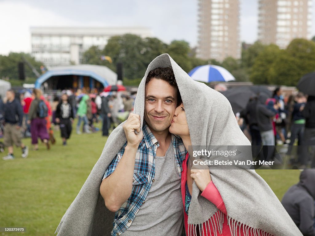 Couple hiding under blanket for rain at festival.