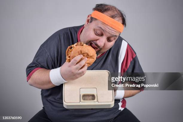 overweight man eating burger on weight scale as plate - man open mouth stock pictures, royalty-free photos & images