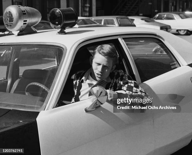 American actor Ron Howard driving a police car on the set of the television sitcom 'Happy Days', USA, circa 1978.