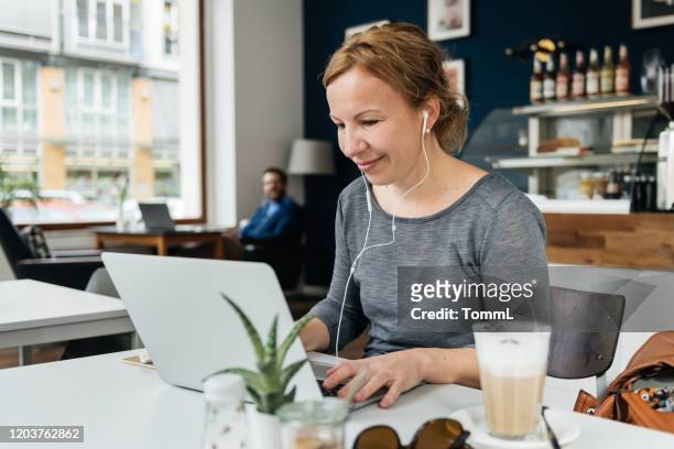 woman listening to music while working in small cafe - lunch and learn stock pictures, royalty-free photos & images