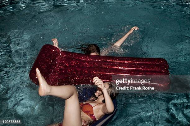 two teenage girls jumping off air mattress in pool - girl jumping stockfoto's en -beelden