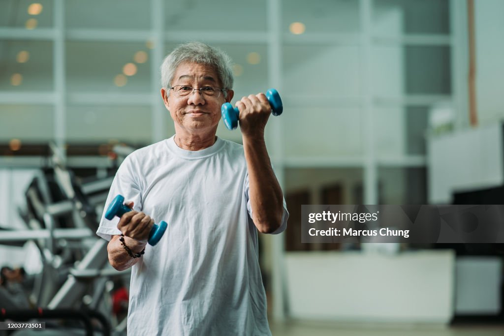 Asian chinese active senior male exercising and workout with dumbbell in gym room during weekend activity