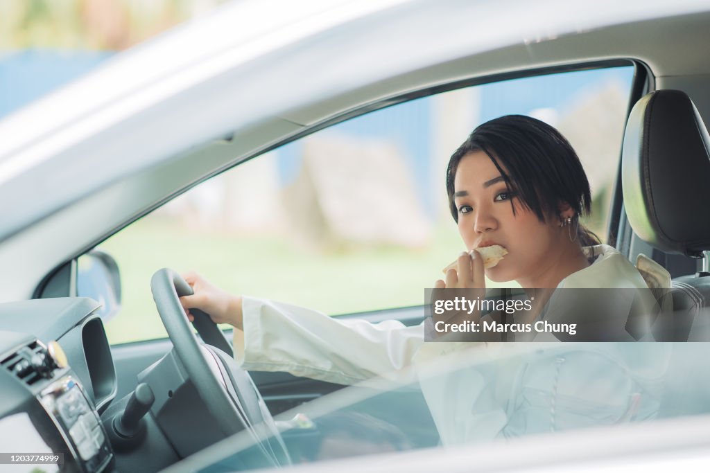 Asian chinese teenager female taxi driver eating sandwiches in her car