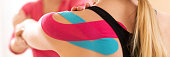 Kinesiology, physical therapy, rehabilitation banner. Female patient wearing kinesio tape on her shoulder exercising with a professional physical therapist. Close up.