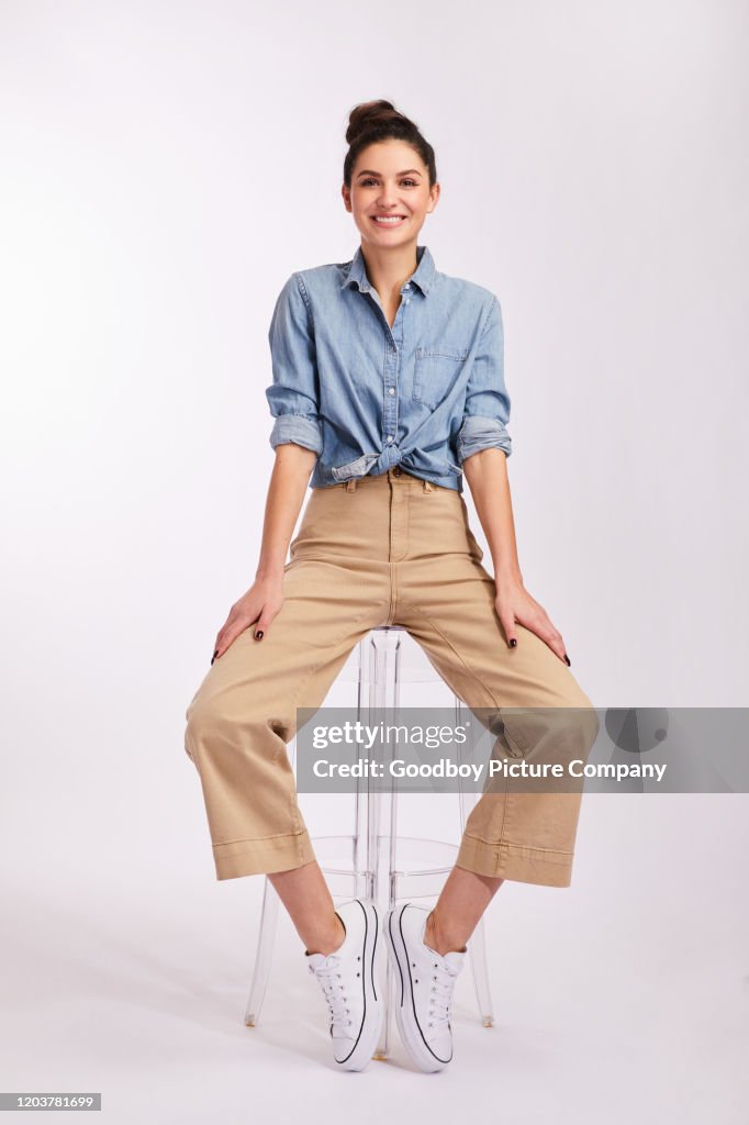 Smiling young brunette woman sitting on a stool on gray